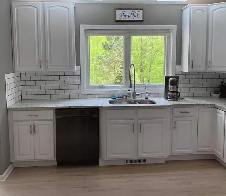 Painted kitchen cabinets with a white finish, subway tile backsplash, black dishwasher, and window above the sink.