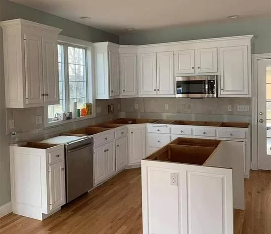 A professional kitchen cabinet refinishing project showing newly painted white cabinets and a clean kitchen layout.